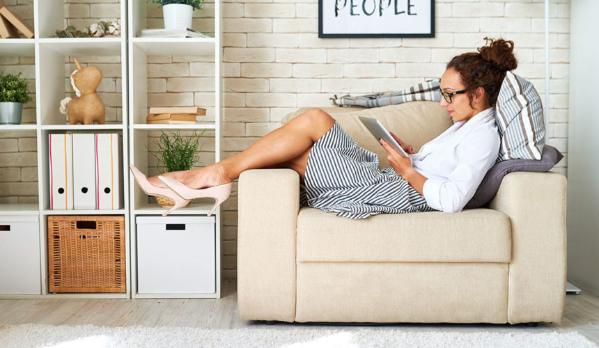 Bien vivre le confinement femme lisant sur un ipad depuis son canapé